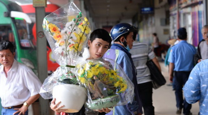 Anh Phạm Văn Thành (21 tuổi, quê Bình
Phước) lỉnh kỉnh ôm hai chậu hoa mai nhựa về biếu gia đình chưng tết - Ảnh: HỮU KHOA