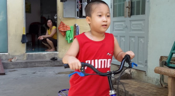 Bé Trần Minh Quang, 6 tuổi, con trai lớn của cô giáo Trần Thị Thêm (người ngồi gần cửa phòng trọ), vui sướng khi được cưỡi lên chiếc xe đạp mini mới tinh - Ảnh: H.Chơn