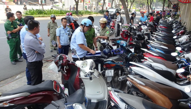 Lực lượng chức năng lập biên bản xử phạt một cửa hàng cho xe máy của khách đậu tràn ra vỉa hè - Ảnh: Lê Phan