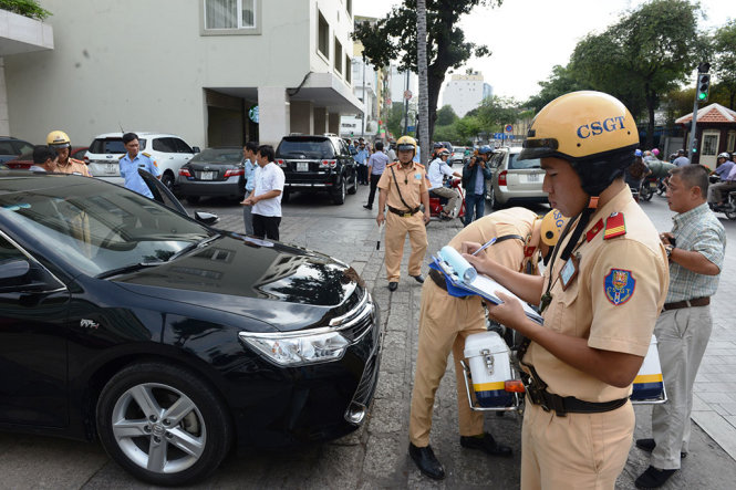 Lực lượng chức năng lập biên bản một xe ôtô đậu trên vỉa hè đường Lê Thánh Tôn (Q.1, TP.HCM) - Ảnh: LÊ PHAN