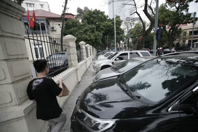 Một người phải lách đi tại một bãi giữ xe ô tô chiếm chọn vỉa hè trên đường Ngô Quyền