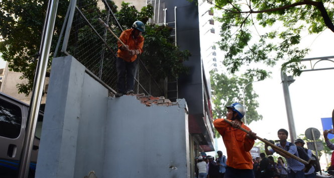 Công nhân phá dỡ bức tường lấn vỉa hè trước tòa nhà số 45 Đinh Tiên Hoàng, Q.1 - Ảnh: HỮU THUẬN