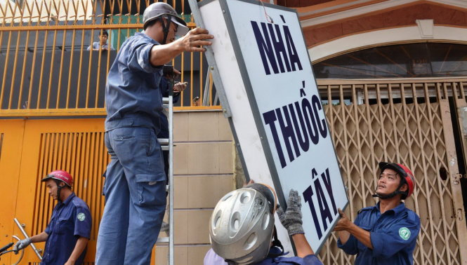 Lực lượng công ích quận 1 tháo dở bảng hiệu lấn chiếm vỉa hè trên đường Nguyễn Đình Chiểu - Ảnh: Lê Phan