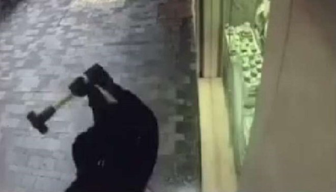 Tên cướp đang đập cửa kính để lấy nhẫn kim cương - Ảnh chụp từ clip