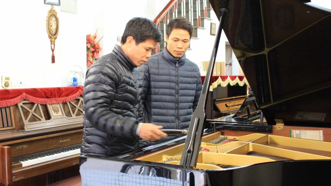 Thợ lên dây dương cầm Đỗ Văn Nhương (trái) và em trai của mình - cũng là một thợ lên dây - đang chăm sóc cho một cây dương cầm của khách hàng - Ảnh: Hà Thanh