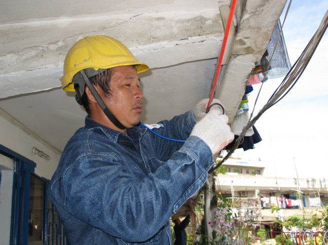 Thợ điện trẻ lắp đặt các bóng đèn tiết kiệm điện tại một khu chung cư - Ảnh: K.Anh