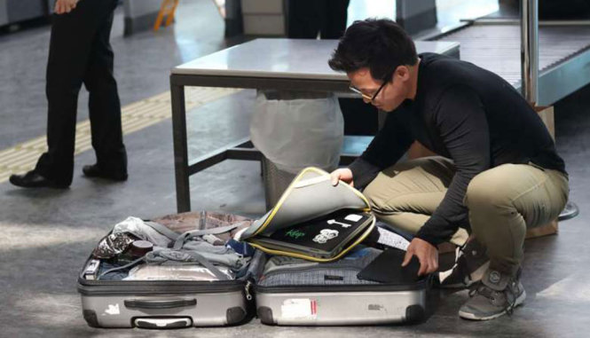 Một hành khách lấy thiết bị điện tử lớn ra khỏi hành lý tại khu vực kiểm tra an ninh của sân bay - Ảnh: EPA