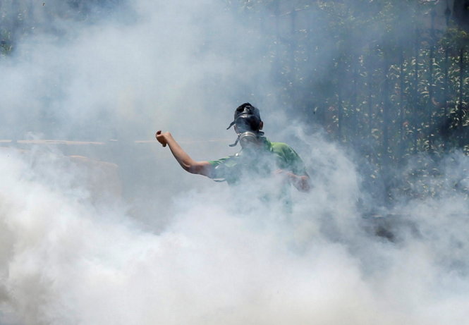 Giữa làn khói đạn cay, người biểu tình mang mặt nạ ném đá về phía cảnh sát Israel trong cuộc xuống đường ngày 17-4 ở Bethlehem - Ảnh: Reuters
