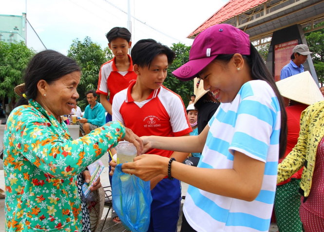 Chủ một tiệm thuốc bắc nhờ các em nhỏ phát trà đá miễn phí cho các hộ dân đang chờ nhận quà hỗ trợ bên ngoài trụ sở UBND xã Mỹ Hội Đông - Ảnh: CHÍ QUỐC