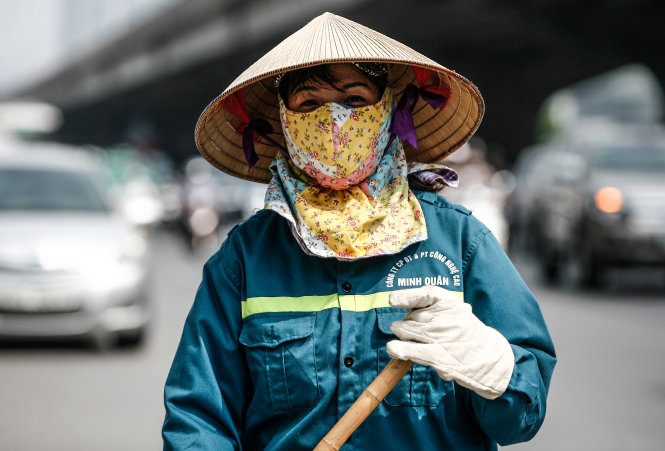 Một công nhân vệ sinh môi trường bịt kín người làm việc dưới trời nắng giữa trưa trên đường vành đai 3 - Ảnh: NAM TRẦN