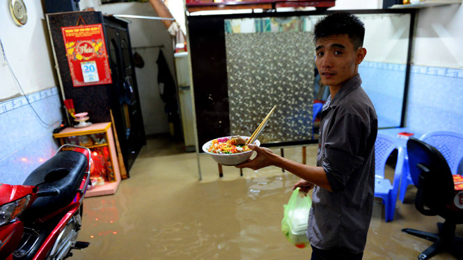 Người dân mua thức ăn về ăn do mưa lớn nước tràn vào nhà gây ngập bếp ăn - Ảnh: HỮU KHOA