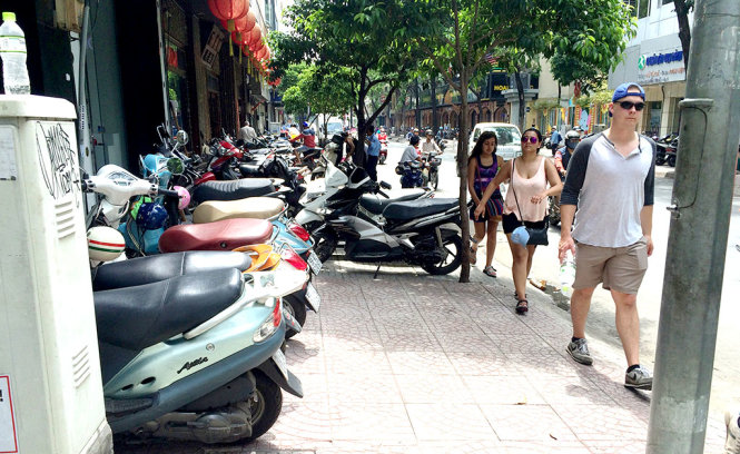 Du khách nước ngoài phải đi né ra đường do xe máy một hộ dân để chắn hết vỉa hè đường Nguyễn Trãi, quận 1- Ảnh: LÊ PHAN