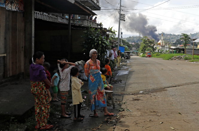 Những người dân ở Marawi bình thản trụ lại giữ nhà trong khi xa xa là cột khói bốc lên do rocket quân đội tấn công nhóm phiến quân - Ảnh: Reuters