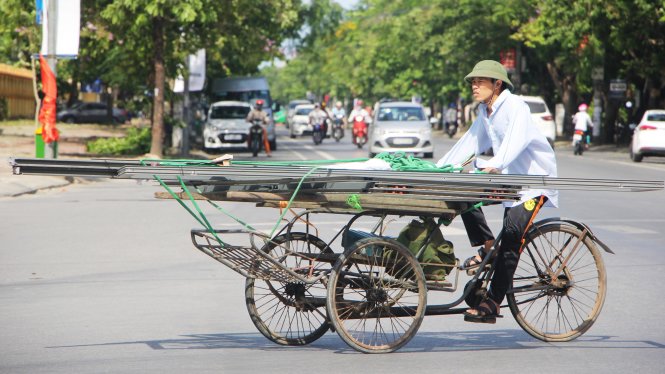 Một người đàn ông đạp xích lô chở thuê hàng mệt nhọc trên đường phố do nắng nóng - Ảnh: Doãn Hòa