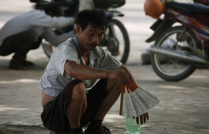 Một người đàn ông vẻ mặt bơ phờ dùng quạt để cho khỏi nóng trên đường Phạm Văn Đồng
