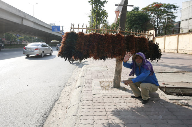 Bất chấp trời nóng, một người đàn ông vẫn ngồi bán chổi lông gà trên đường Khuất Duy Tiến, Hà Nội - ẢNH: Nam Trần