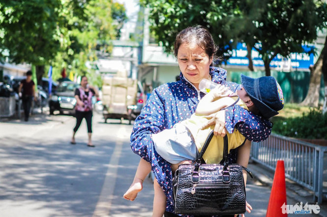 Một người phụ nữ đang bế một đứa trẻ di chuyển vội vã trong nắng nón - Ảnh: Nguyễn Khánh