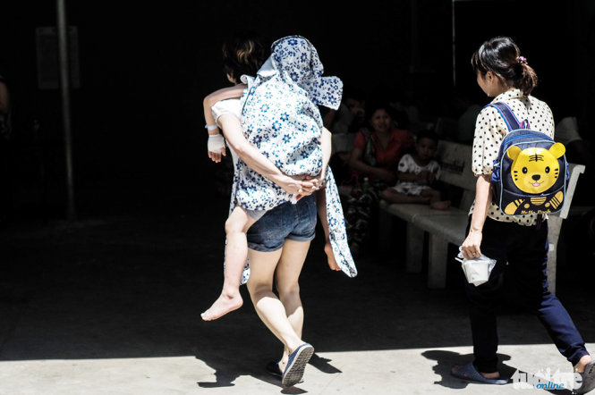 Một bệnh nhi mặc áo chống nắng và được mẹ cõng trên lưng để đi khám bệnh - Ảnh: Nguyễn Khánh