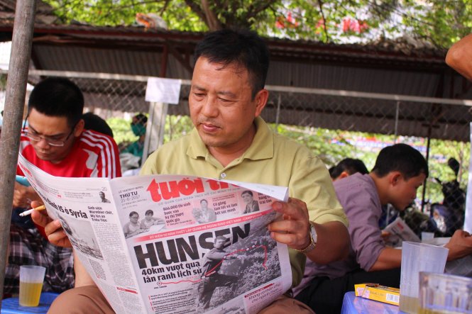 Một phụ huynh tại điểm thi Trường ĐH Công nghiệp Hà Nội đang đọc báo Tuổi Trẻ dưới tiết trời oi bức trong lúc chờ con trai làm thủ tục dự thi - Ảnh: Hà Thanh