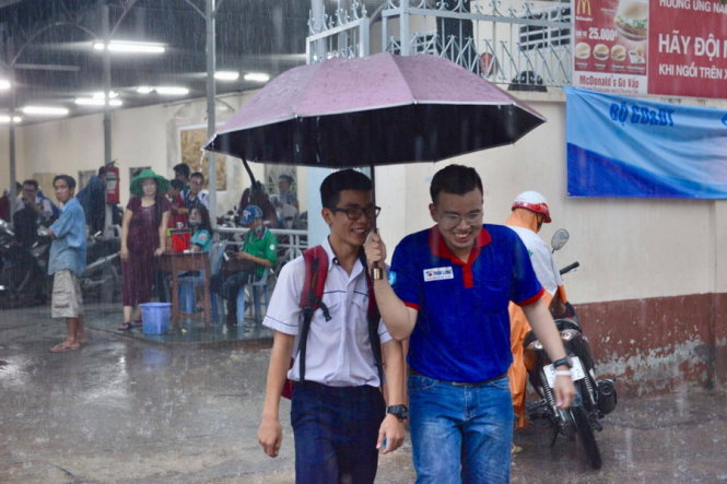 Trời bất ngờ đổ cơn mưa lớn, lực lượng tiếp sức mùa thi che dù để đưa các thí sinh ra về tại điểm thi THPT Gia Định,  Q. Bình Thạnh, TP.HCM - Ảnh: Duyên Phan