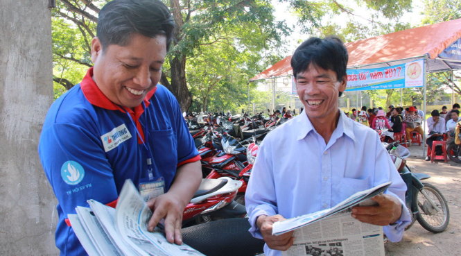 Thầy Vũ (trái) cười tươi tặng báo cho phụ huynh học sinh - Ảnh: Trần Mai