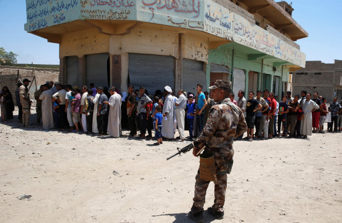 Một binh sĩ Iraq bảo vệ đoàn người đang đứng xếp hàng đợi lãnh nhu yếu phẩm cho ngày lễ Eid al-Fitr ở Mosul ngày 25-6 - Ảnh: Reuters