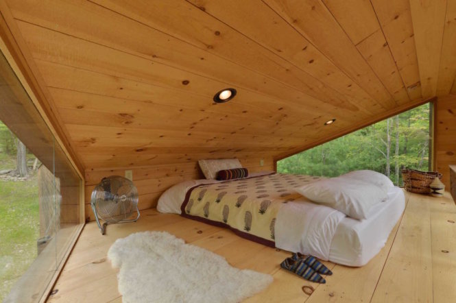 Giường ngủ được đặt vừa vặn với diện tích khiêm tốn của gác lửng. Hai mặt kính tạo cảm giác mở và tầm nhìn đẹp ra cảnh hồ và rừng cây.