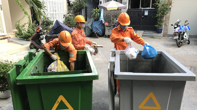 Các công nhân gom rác đã phân loại tại đường Nguyễn Bỉnh Khiêm, Q.1, thùng bên trái màu xanh chứa rác thực phẩm, thùng màu xám chứa rác còn lại - Ảnh: Q.KHẢI
