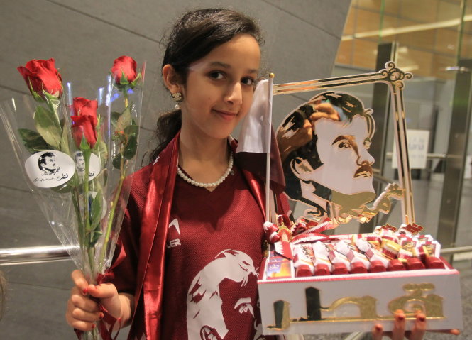 Bé gái người Qatar cầm hoa và ảnh chân dung Quốc vương Sheikh Tamim bin Hamad Al Thani tại sân bay Doha  - Ảnh: Reuters