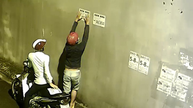 Hai thanh niên dán tờ rơi lên tường nhà dân ở phường Phước Long B, quận 9, TP.HCM - Ảnh cắt từ clip