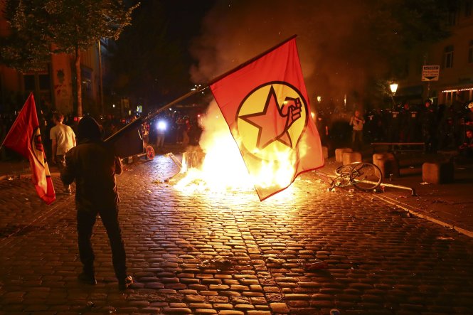 Người biểu tình đứng cạnh các tấm chắn bị đốt cháy trong cuộc biểu tình phản đối hội nghị G20 tại thành phố Hamburg, Đức - Ảnh: Reuters