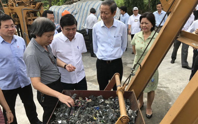 Chủ tịch Nguyễn Thành Phong (giữa) xem rác thải công nghiệp chuẩn bị đưa vào lò gia nhiệt để phát điện của mô hình thử nghiệm ở bãi rác Gò Cát sáng 11-7 - Ảnh Q.Khải