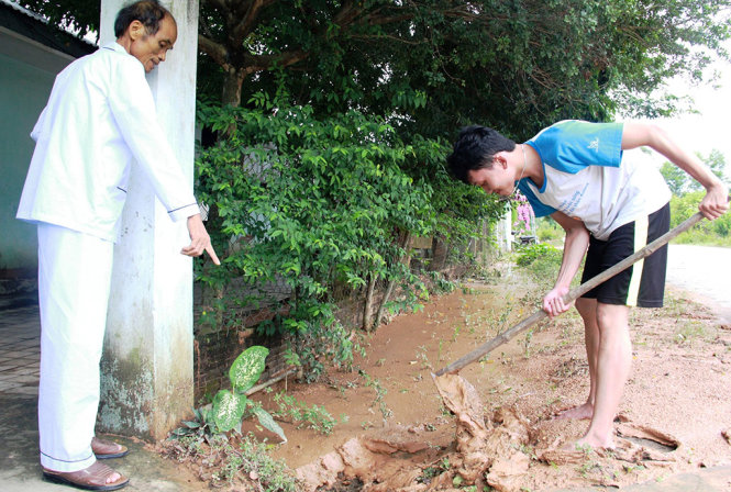 Ông Bình và con trai sau khi dọn bùn trong sân tiếp tục dọn mương sau trận mưa chiều 14-7 - Ảnh: TRẦN MAI