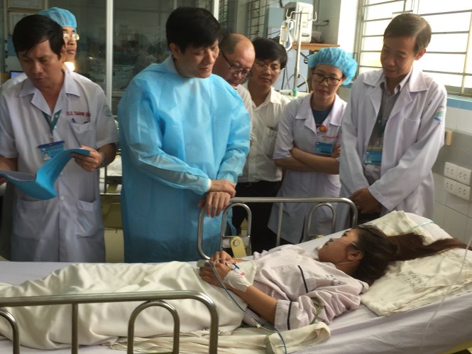 Thứ trưởng Nguyễn Thanh Long (mặc áo choàng của bệnh viện) đang hỏi thăm người bệnh mắc bệnh sốt xuất huyết điều trị ở Bệnh viện Bệnh nhiệt đới, TP.HCM - Ảnh: THUỲ DƯƠNG