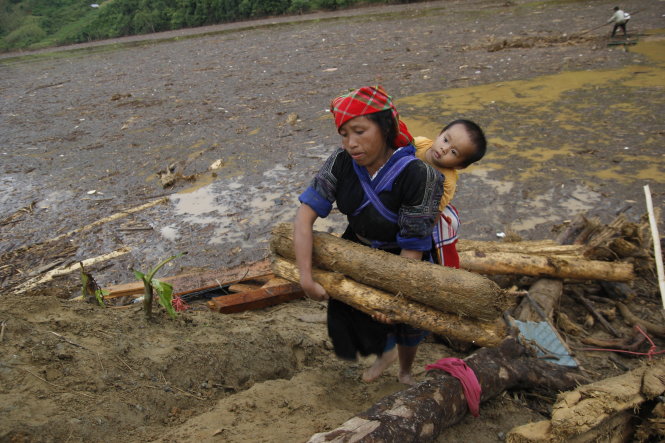 Vừa địu con, chị Hàn Thị Sông, ở thị trấn Mù Cang Chải, vừa chuyển những khúc gỗ từ bờ lên trên mặt đường - ẢNH: Quang Dự