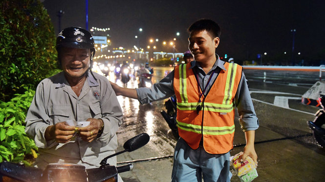 Anh Nguyễn Ngọc Minh, nhân viên cứu hộ đường hầm sông Sài Gòn phát áo mưa miễn phí cho người đi đường - Ảnh: HỮU THUẬN