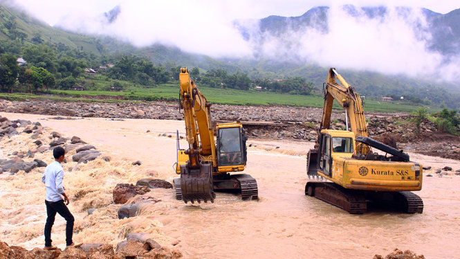 Hai máy cẩu liên tục làm việc tại bờ suối, múc đá chặn dòng nước lũ