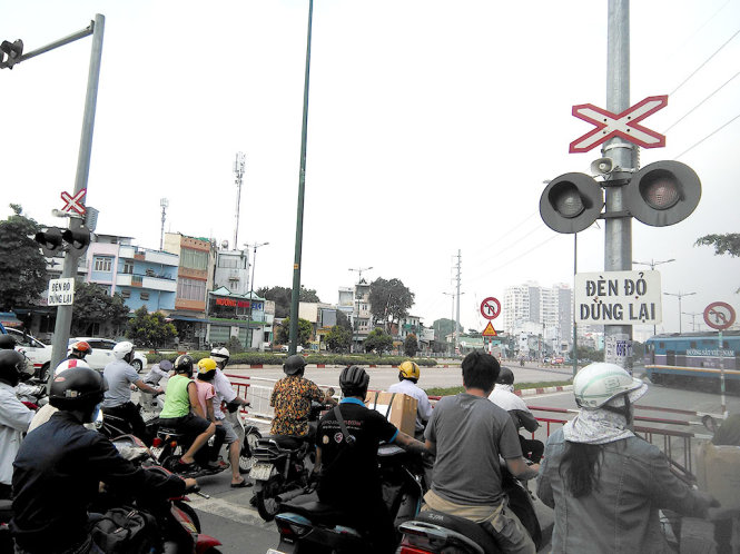 Người đi đường dừng trước đường ngang chờ tàu chạy qua trên đường Phạm Văn Đồng, TP.HCM sáng 12-8. - Ảnh: ĐỨC PHÚ