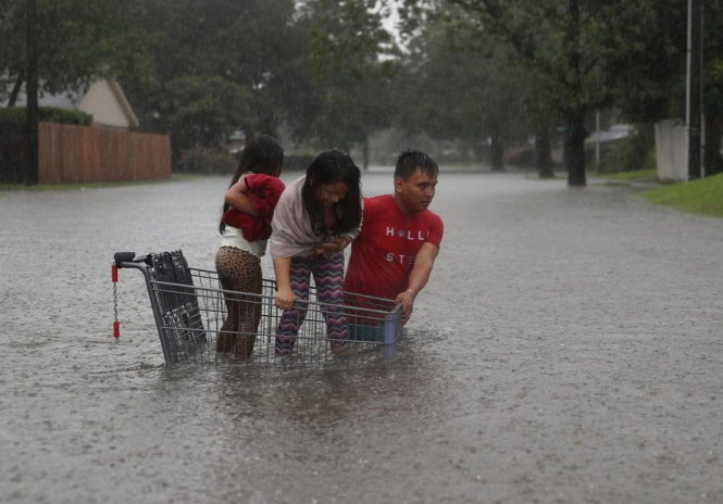 Người cha gốc Việt dùng xe đẩy siêu thị đưa con qua con đường ngập nước ở Houston - Ảnh: AFP