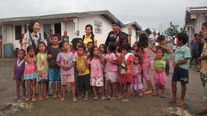 Bà Thanh Thư (bìa trái) và đoàn phim cùng những đứa trẻ sống sót sau cơn bão Haiyan, phía sau là dãy nhà tạm do quốc tế tài trợ cho những người bị mất nhà sau cơn bão - Ảnh: VTV