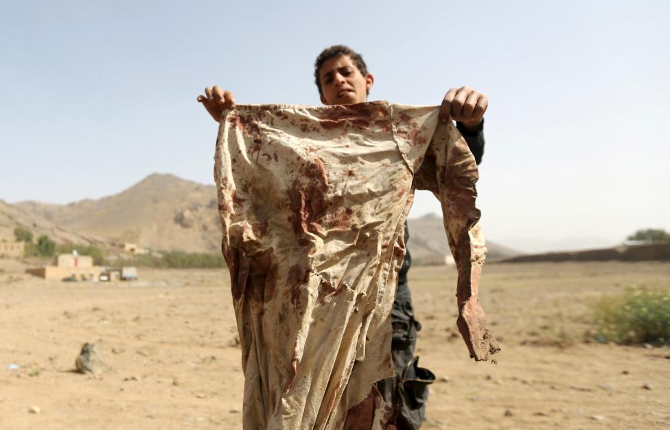 Một cậu bé cầm một chiếc áo vấy máu tại một khu vực diễn ra một cuộc không kích vào một ngôi nhà trong làng Bait Regal ở phía tây của thủ đô Sanaa của Yemen ngày 7-4-2015. Phương tiện truyền thông địa phương đưa tin ba phụ nữ và ba trẻ em trong một gia đình đã bị giết chết sau cuộc không kích - Ảnh: Khaled Abdullah