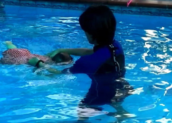 Cô T. dùng tay nhấn đầu một bé 2 tuổi để bé úp mặt xuống nước học bơi - Ảnh: Quang Phương cắt từ clip