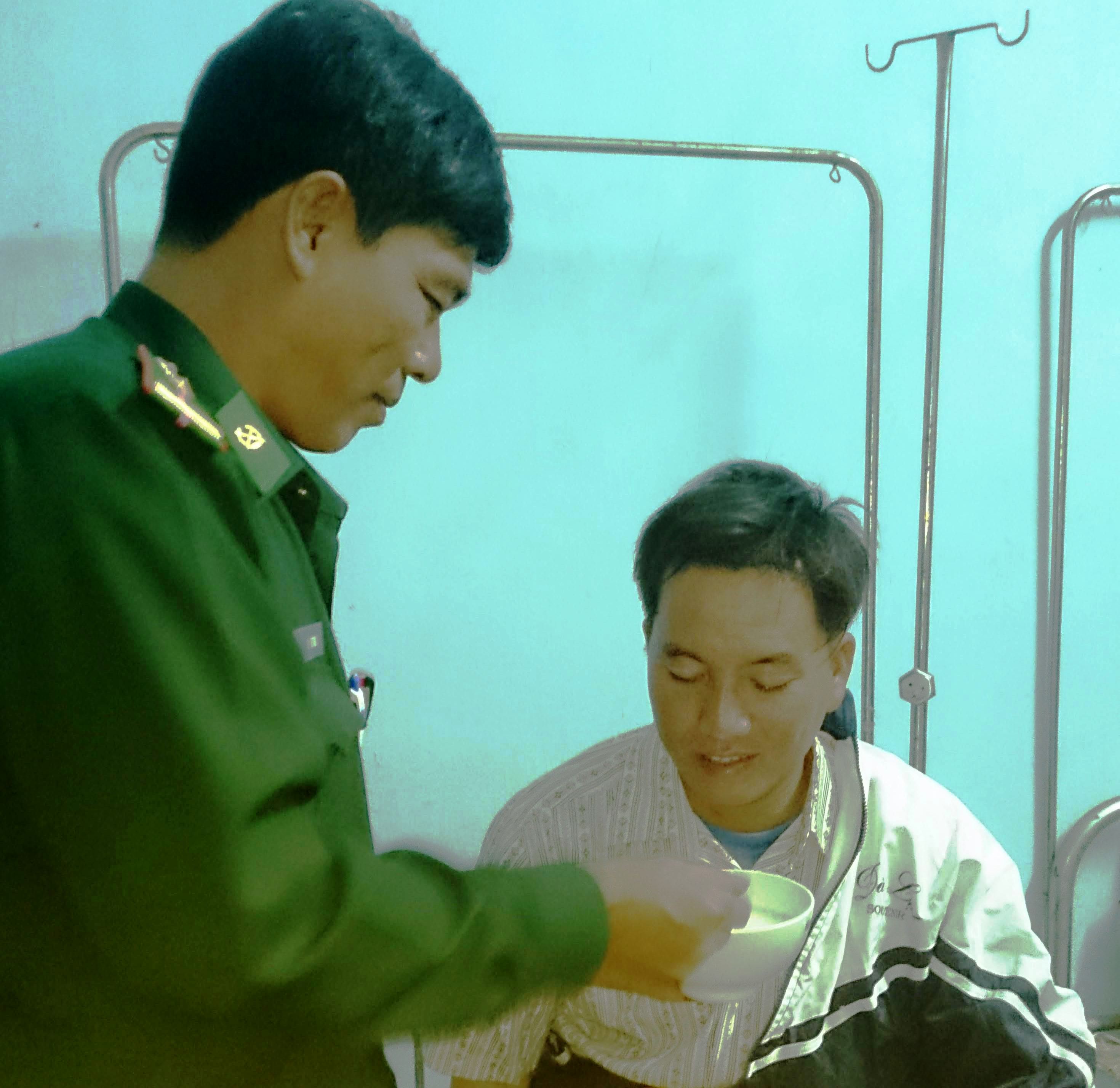 Ngư dân Nguyễn Văn Lộc (ngồi) được bộ đội biên phòng bón cháo tại trạm y tế xã Phổ Khánh  - Ảnh: HỒ NGỌC HÀN