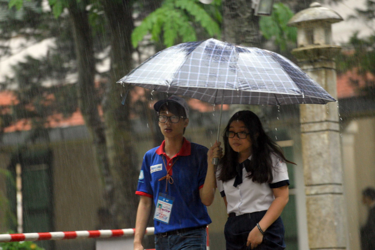 Sinh viên tình nguyện đội mưa đưa thí sinh ra về sau khi làm thủ tục dự thi tại điểm thi trường THPT Lê Quý Đôn - Ảnh: HỮU KHOA