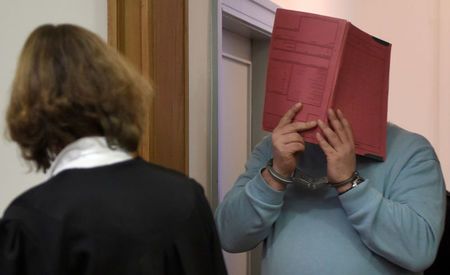 Cựu y tá Niels Hoegel dùng tấm bìa che mặt trong một phiên xử ở Oldenburg năm 2014 - Ảnh: Reuters